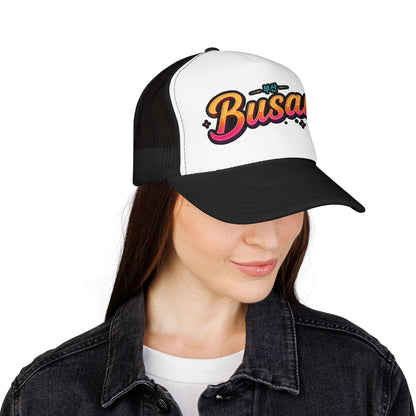 Two-tone trucker hat side view: white front with Busan logo, black mesh panels, curved brim.