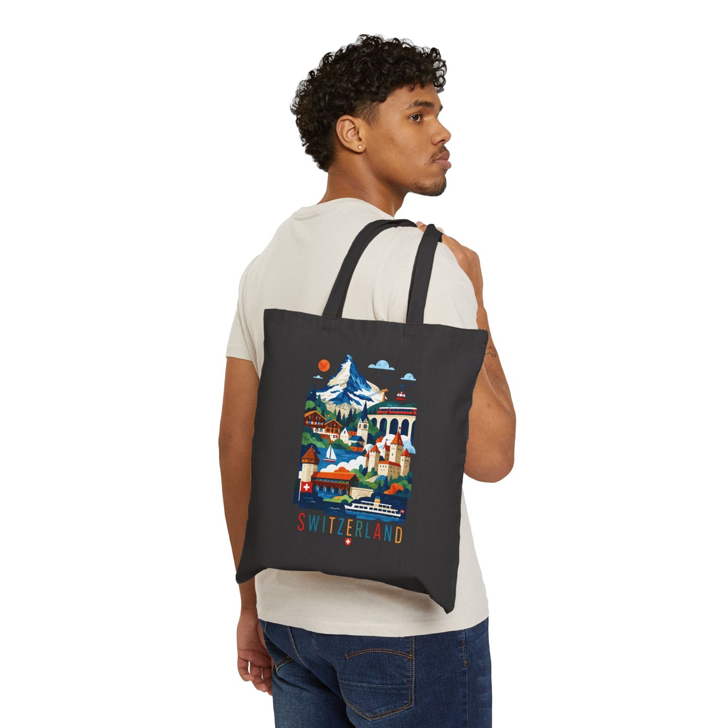 Black canvas tote bag with Switzerland scenic print, carried on a man’s shoulder.