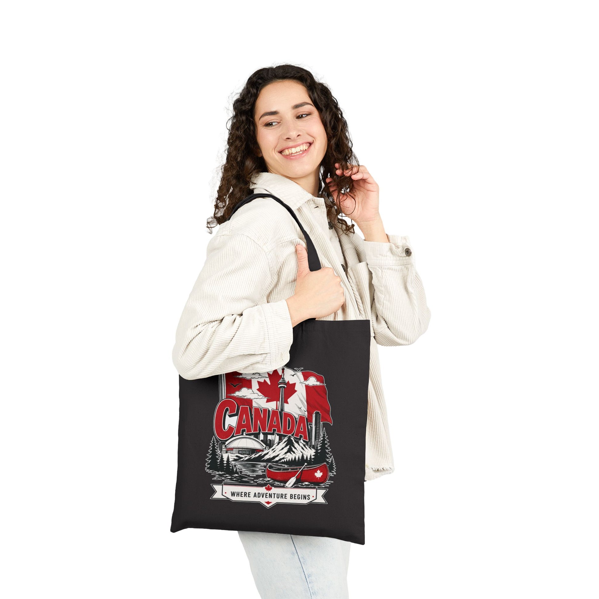 Black canvas tote bag with Canada flag canoe graphic, carried in hand