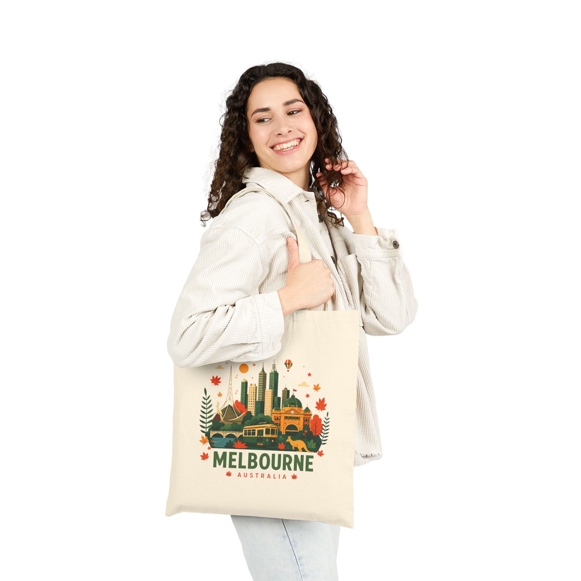 Natural canvas tote bag worn by person, front shows Melbourne city graphic.
