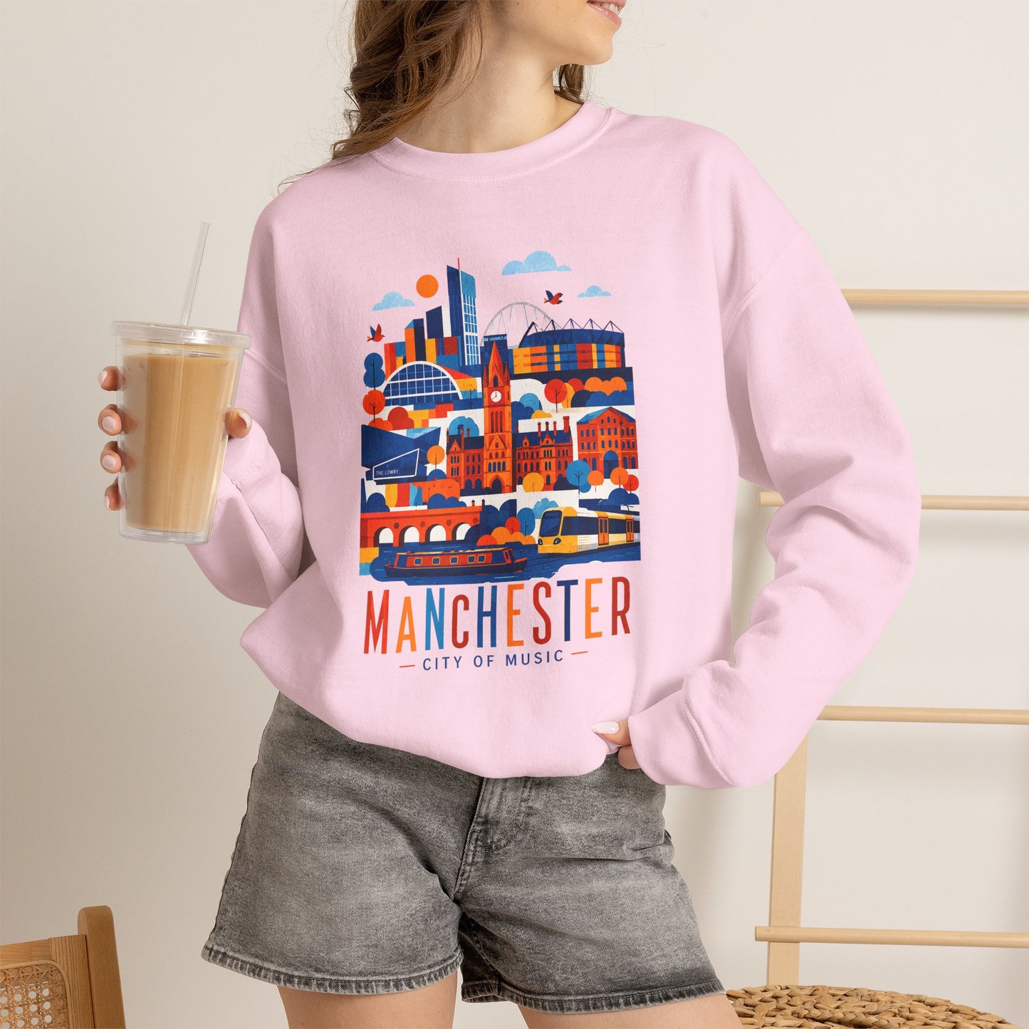 Light pink crewneck sweatshirt worn by model, cityscape graphic with Manchester text