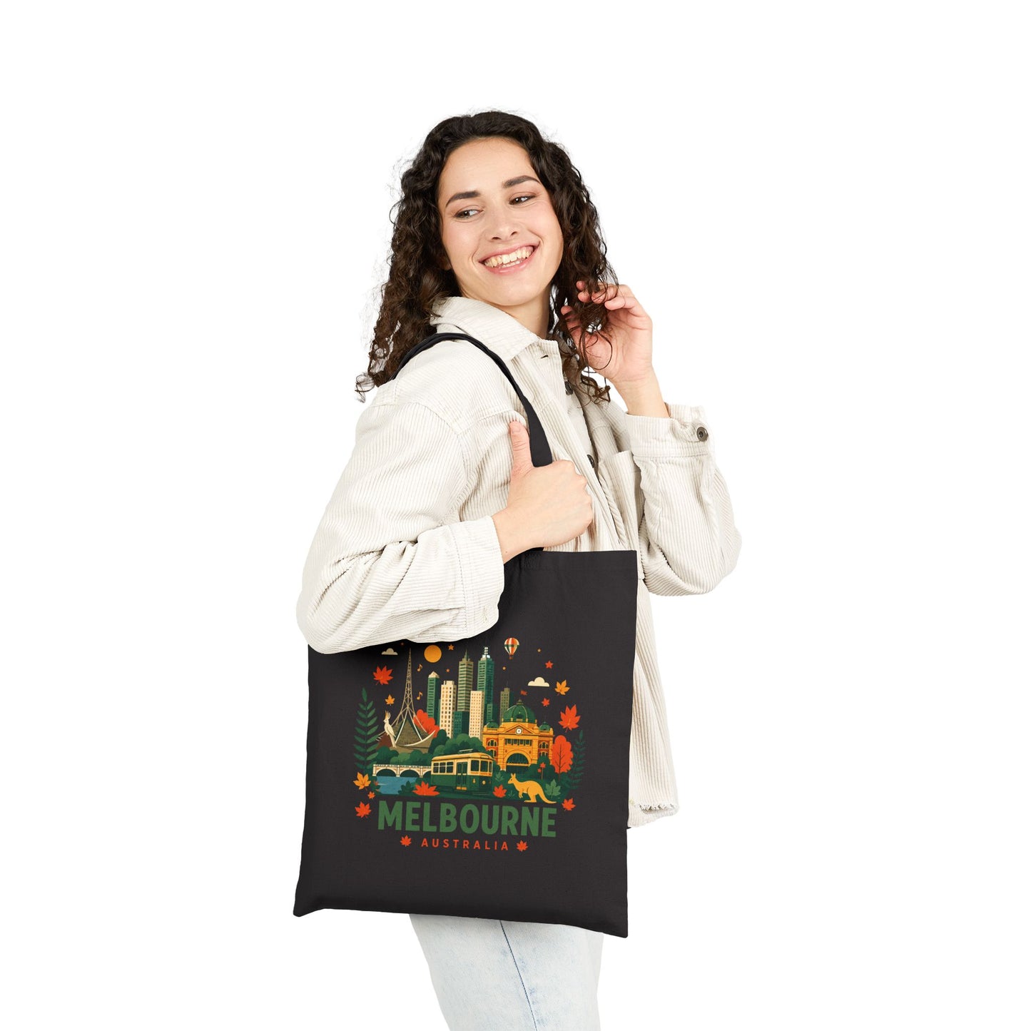Black canvas tote bag worn by person, front shows Melbourne city graphic.