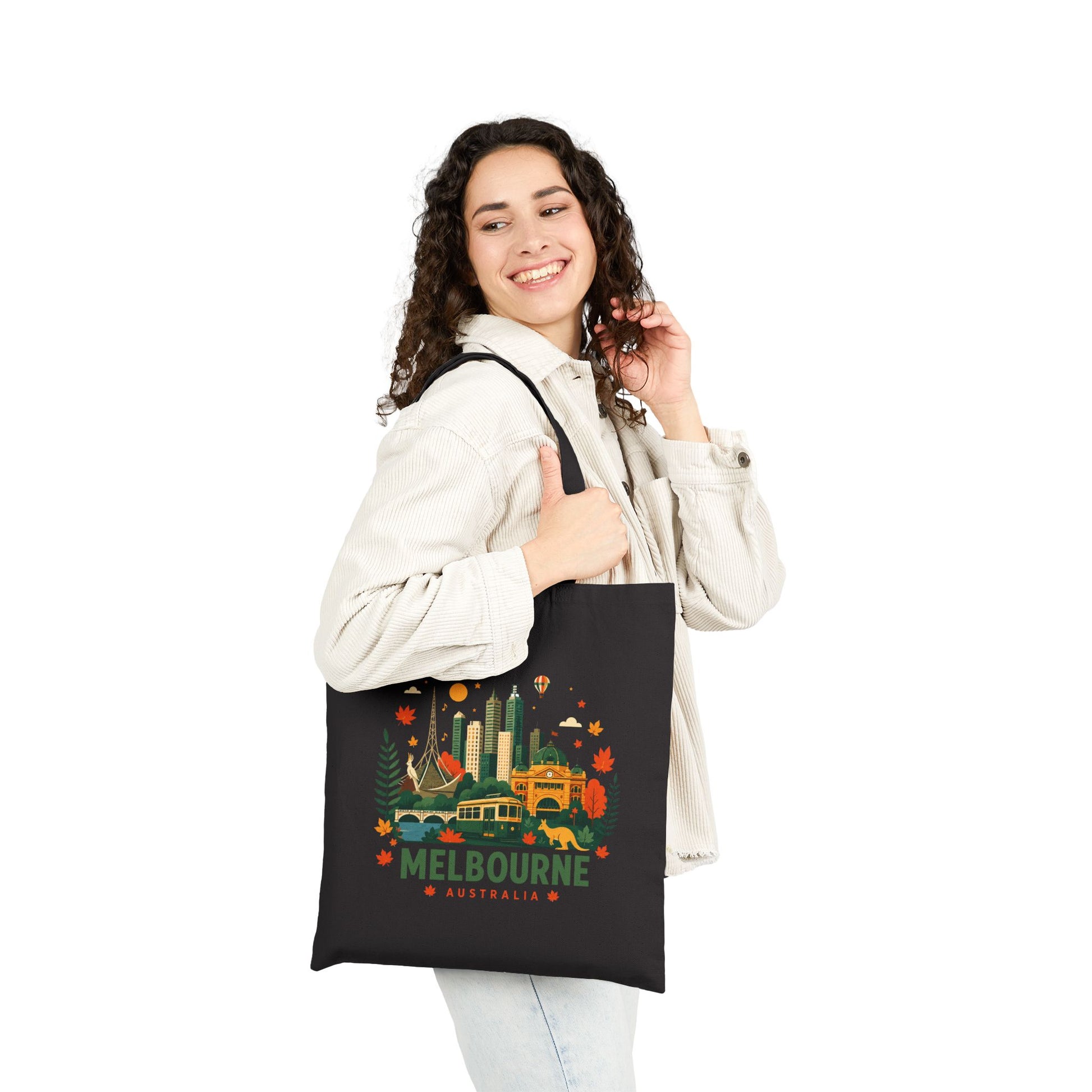 Black canvas tote bag worn by person, front shows Melbourne city graphic.