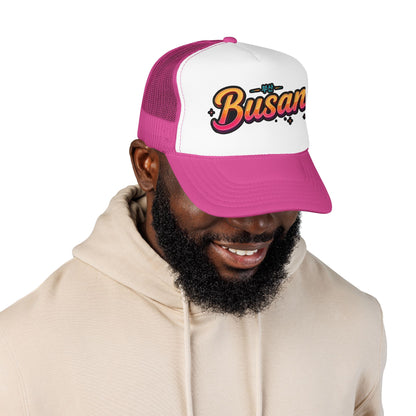 Pink and white trucker hat with front Busan logo, worn by a person