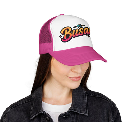 Pink and white trucker hat with front Busan logo, worn by a person