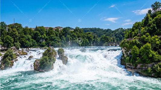 Desktop wallpaper featuring wide waterfall with rocky riverbanks and forested greenery