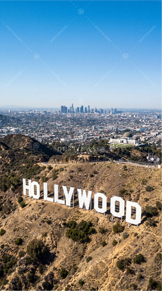 Hollywood sign on grassy hillside with distant city skyline, USA mobile wallpaper